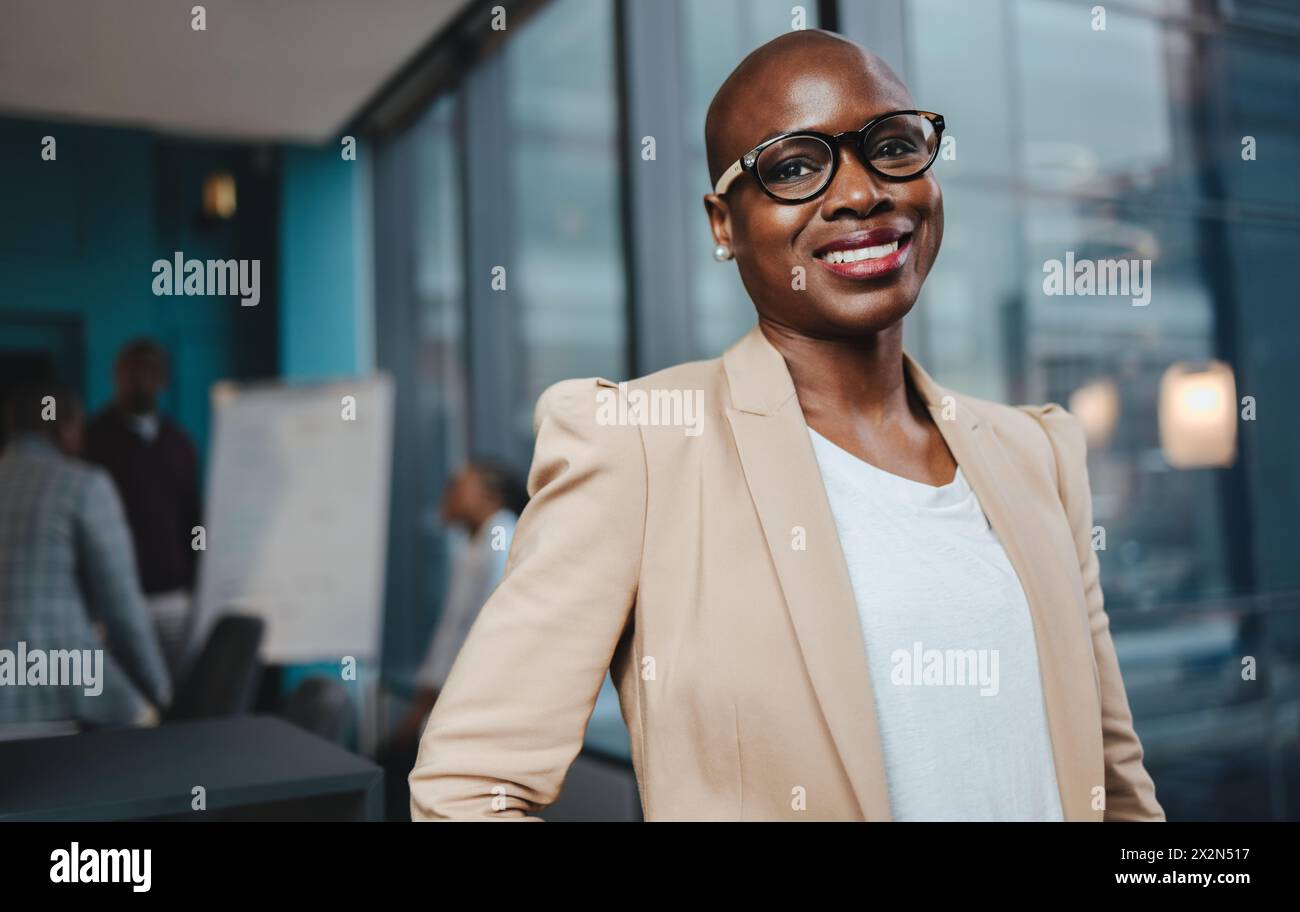 Portrait of a businesswoman in a boardroom office. She stands, smiling and looking at the camera, portraying success and professionalism. A mature fem Stock Photo
