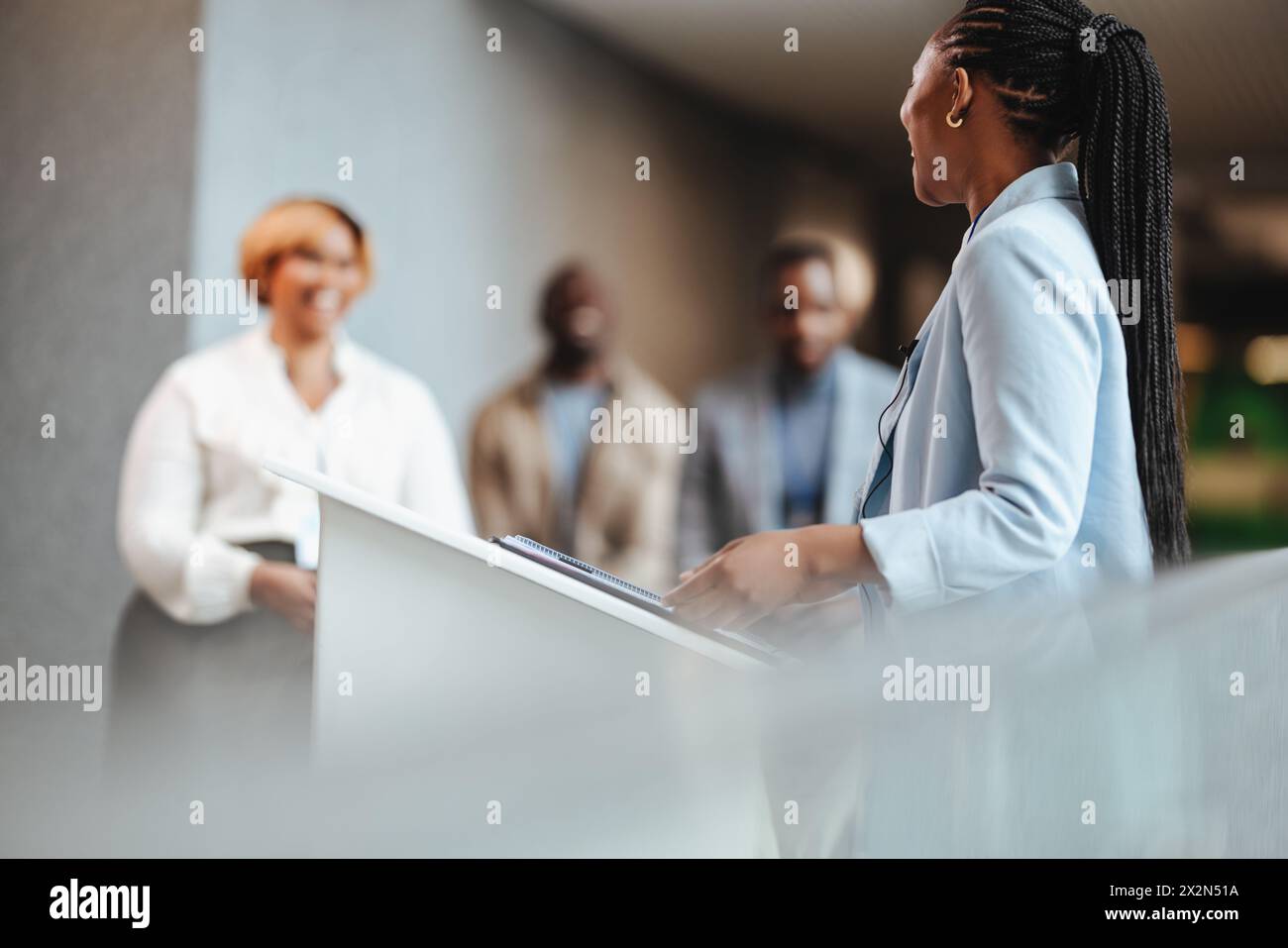 Young businesswoman confidently presenting at a podium during a corporate event. Female professional engaging an audience of entrepreneurs, depicting Stock Photo