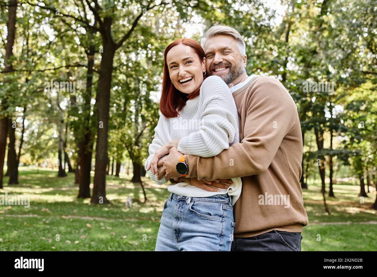 A man and a woman share a warm hug among the serene surroundings of a park. Stock Photo