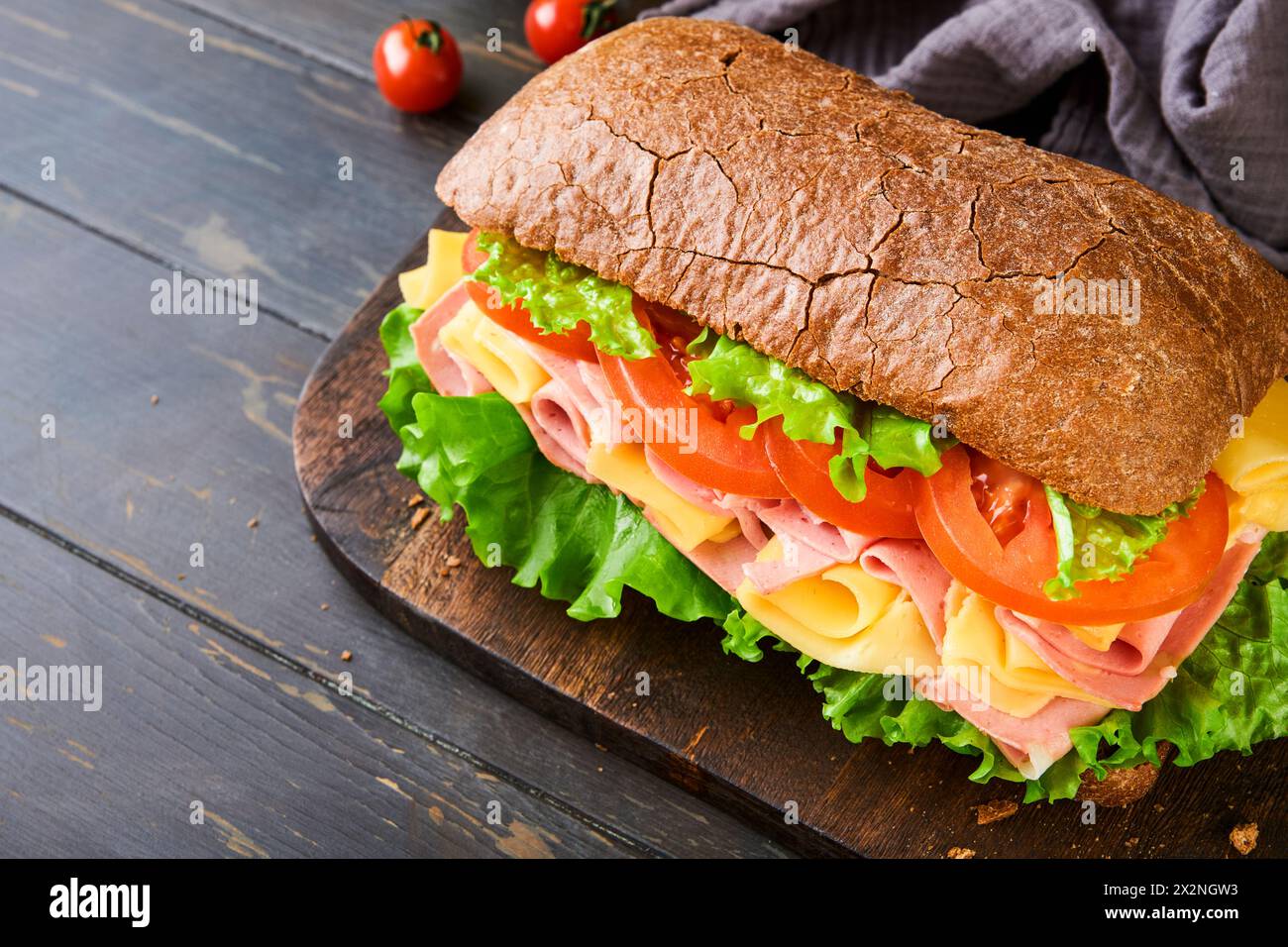 Sandwich. One fresh big submarine sandwich with ham, cheese, lettuce, tomatoes and microgreens on old wooden dark background. Healthy breakfast theme Stock Photo