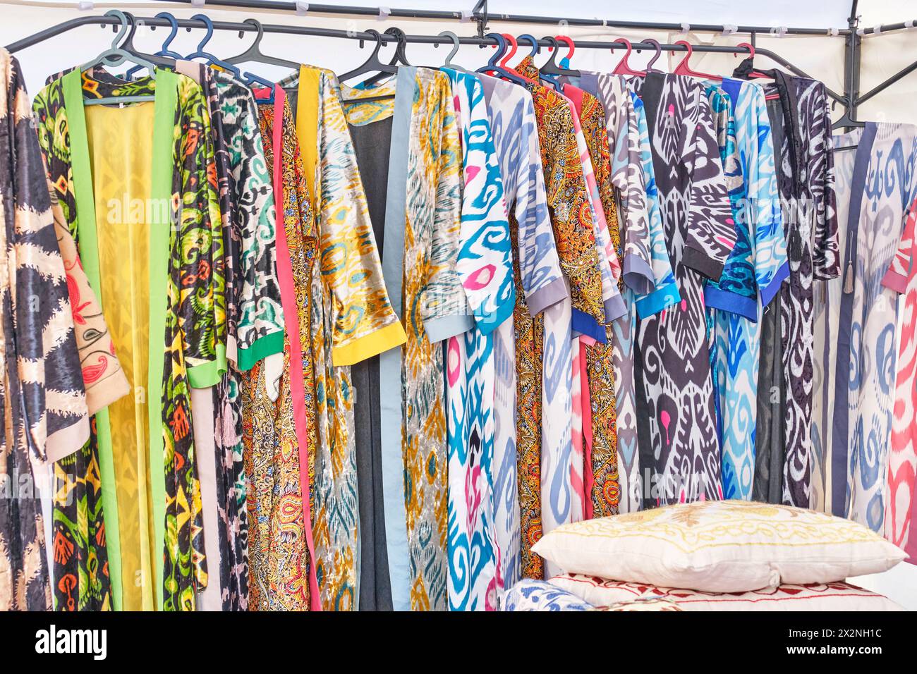 Long women's Central Asian robes with traditional colorful patterns on hangers in a row in a sales tent. Crafts fair on a pedestrian street, Almaty, K Stock Photo