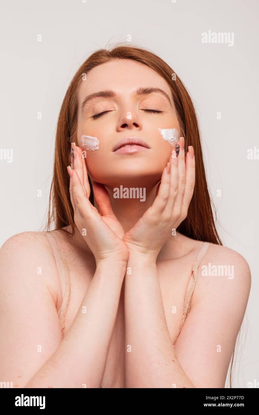 Beautiful Young Redhead Woman In A Beige Bra Does Skin Care And Applies Cream On Her Face Stock Photo