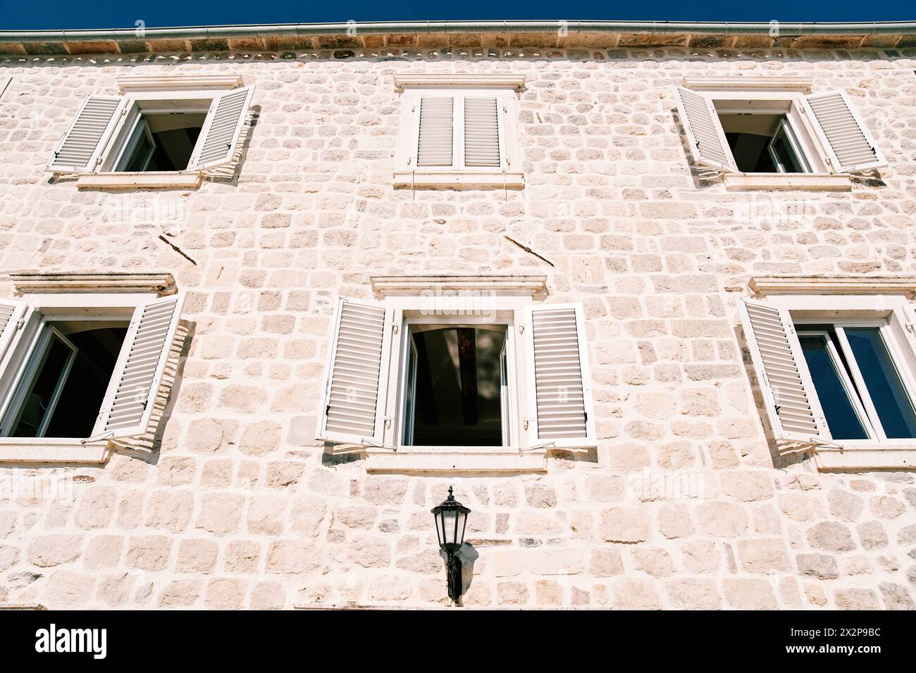 Facade of an old stone mansion with white wooden shutters wide open ...