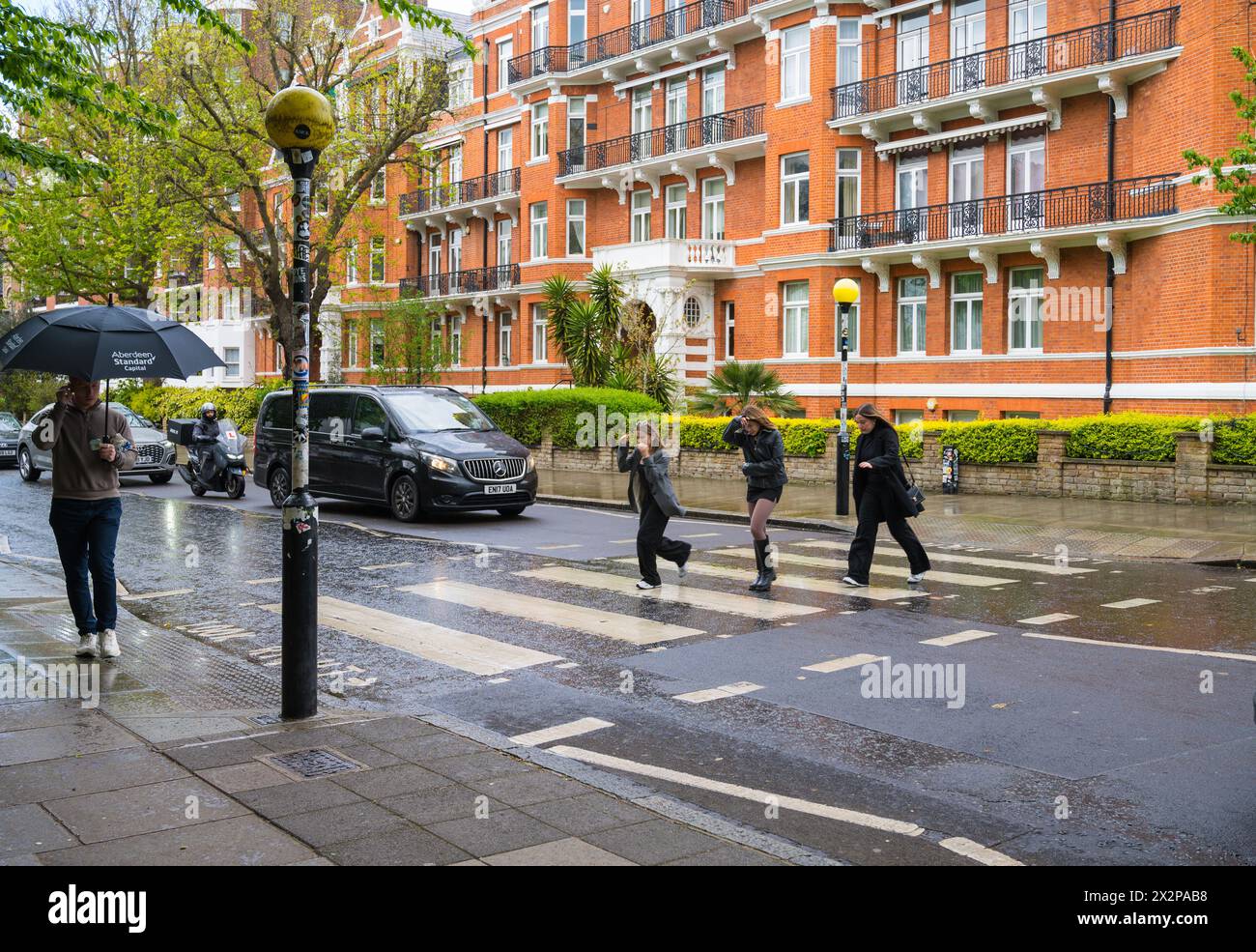 Three young women on the Abbey Road zebra crossing during rain shower ...