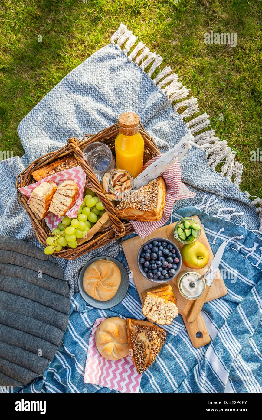 Picnic duvet and basket with different food, fruits, orange juice., yogurt and bread on green grass Stock Photo