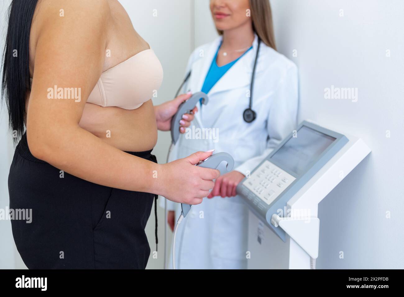A health practitioner assists obese young woman with a body composition test using advanced equipment. Stock Photo