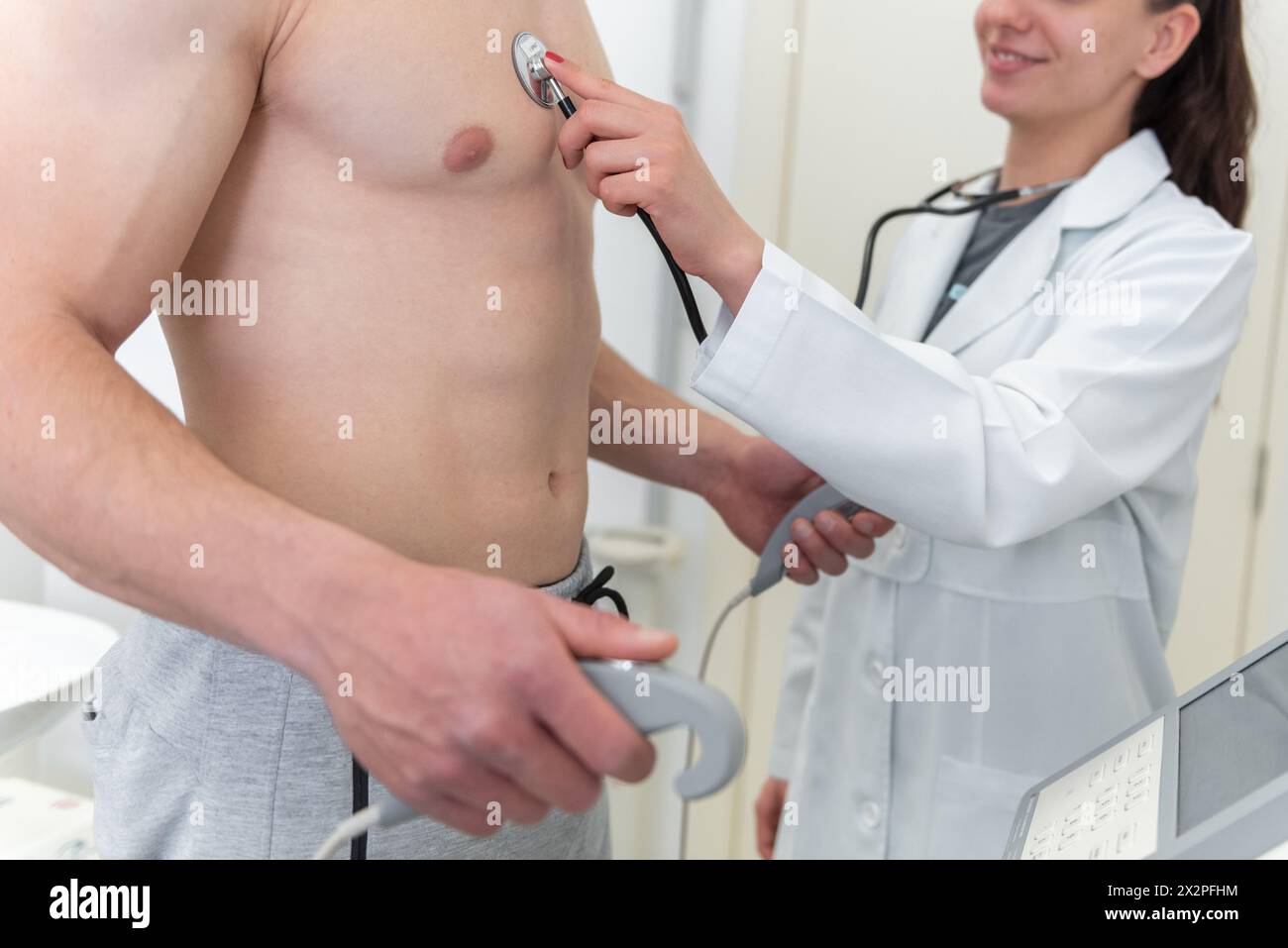 A smiling doctor is using a stethoscope to listen to a patients chest in a medical clinic. Stock Photo