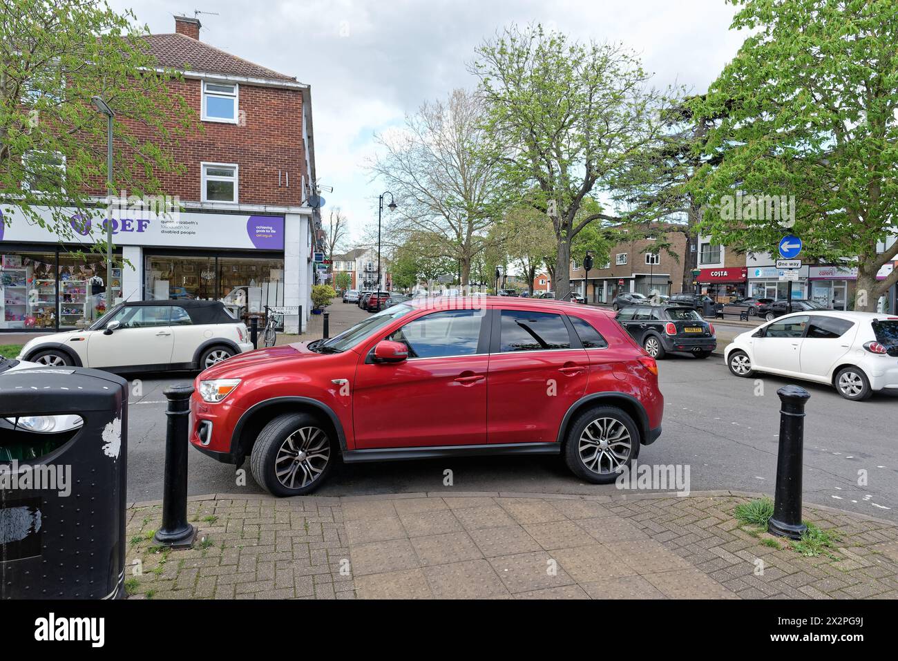 A badly parked car obstructing a dropped kerb on a pavement in a suburban high street