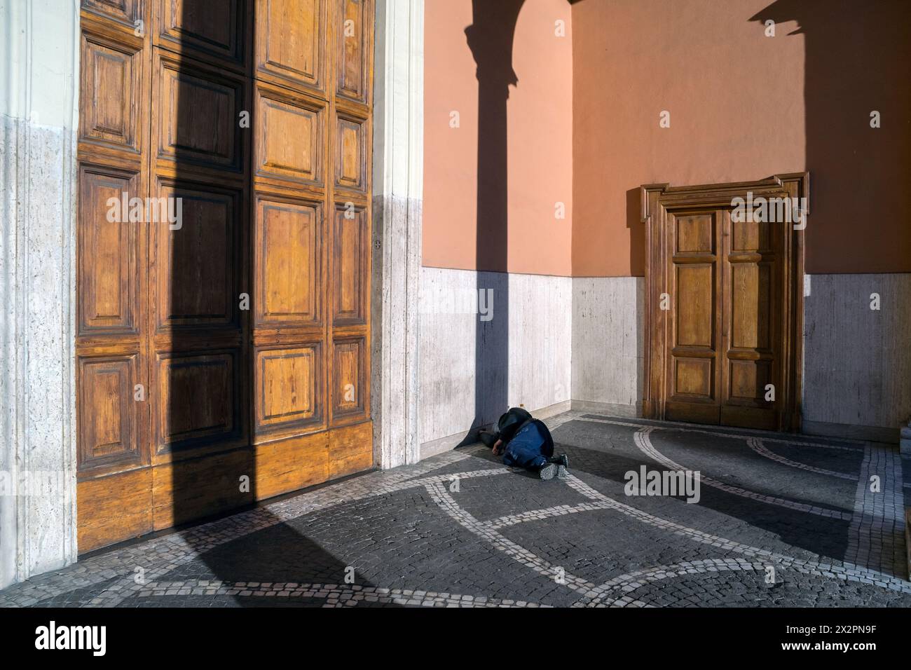Italy, Rome: a homeless man sleeps lying in the shade of a column in front of the entrance to a closed church Stock Photo