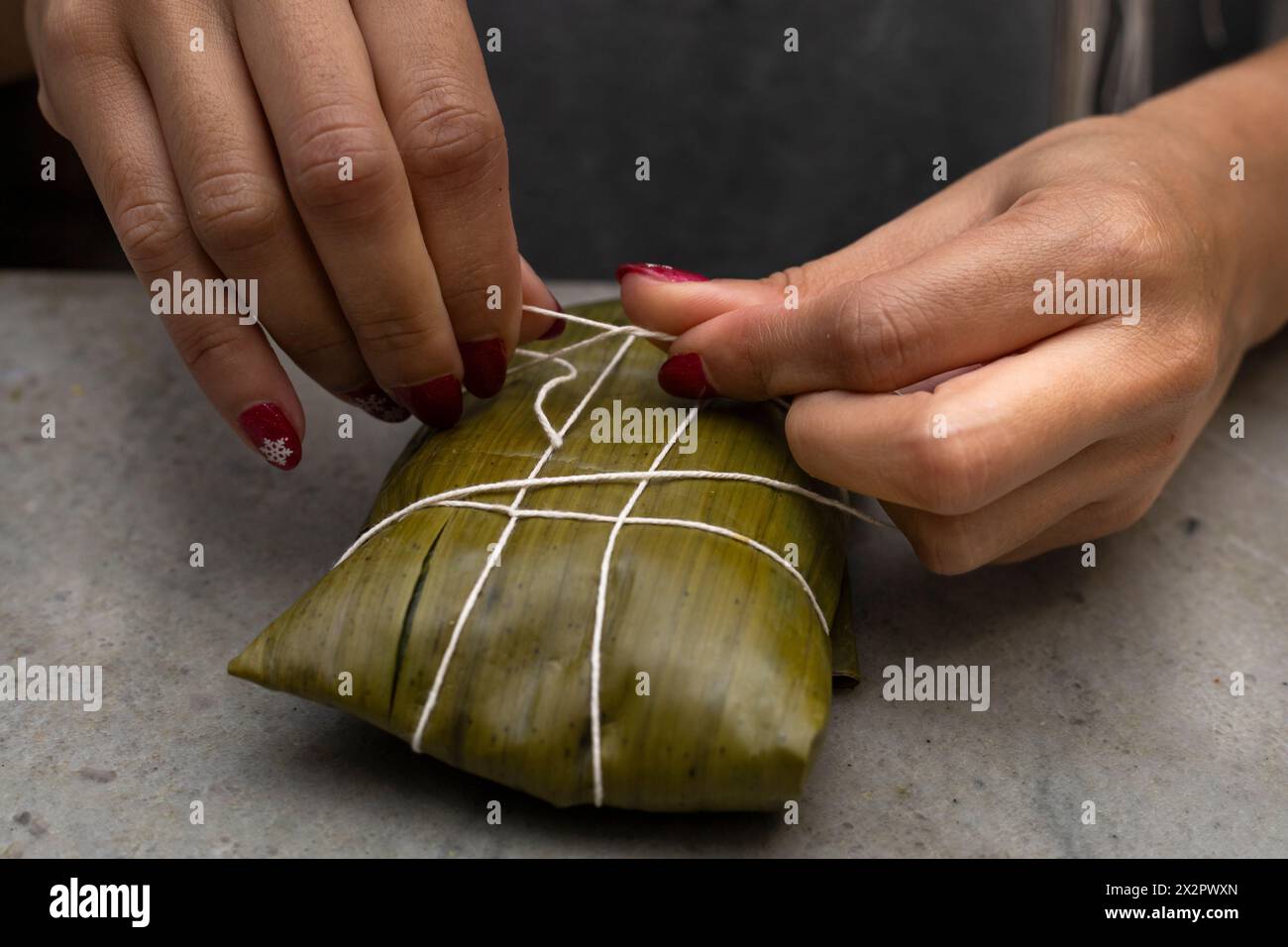 Hallaca Threading Woman's hands tying a hallaca or tamale in a banana leaf. Traditional ...