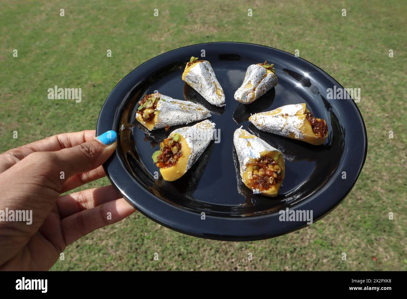 Female holding serving Paan flavoured Indian sweets. Paan barfi stuffed with Gulkand paan flavor. Paan burfi in dish Stock Photo