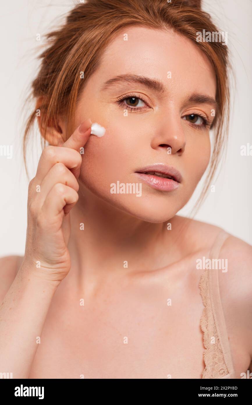Beautiful Young Natural Redhead Lady With Clean Face Skin Applies Cream And Moisturizes The Skin. Beauty And Skin Care Stock Photo
