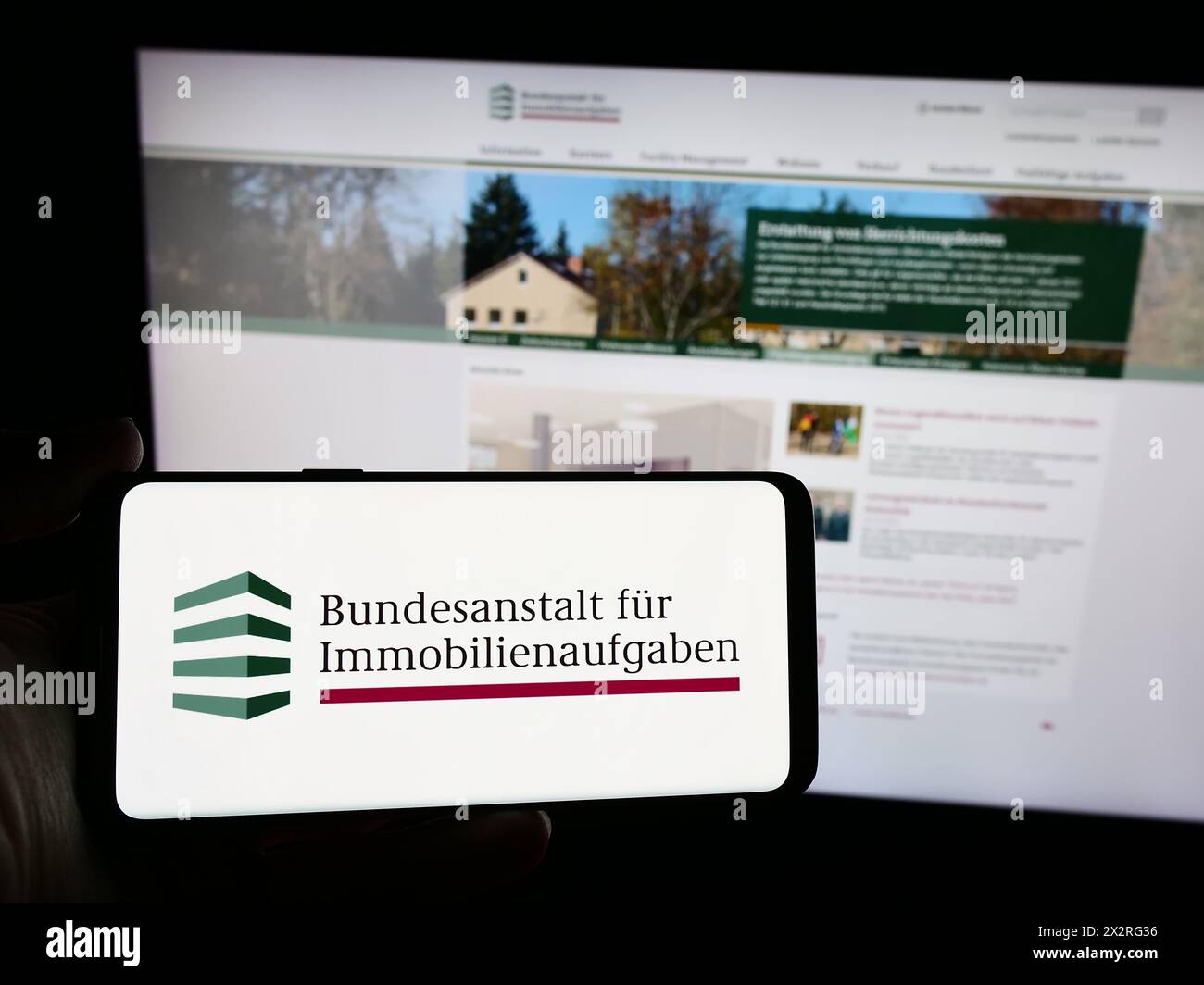 Person holding smartphone with logo of German agency Bundesanstalt für Immobilienaufgaben (BImA) in front of website. Focus on phone display. Stock Photo