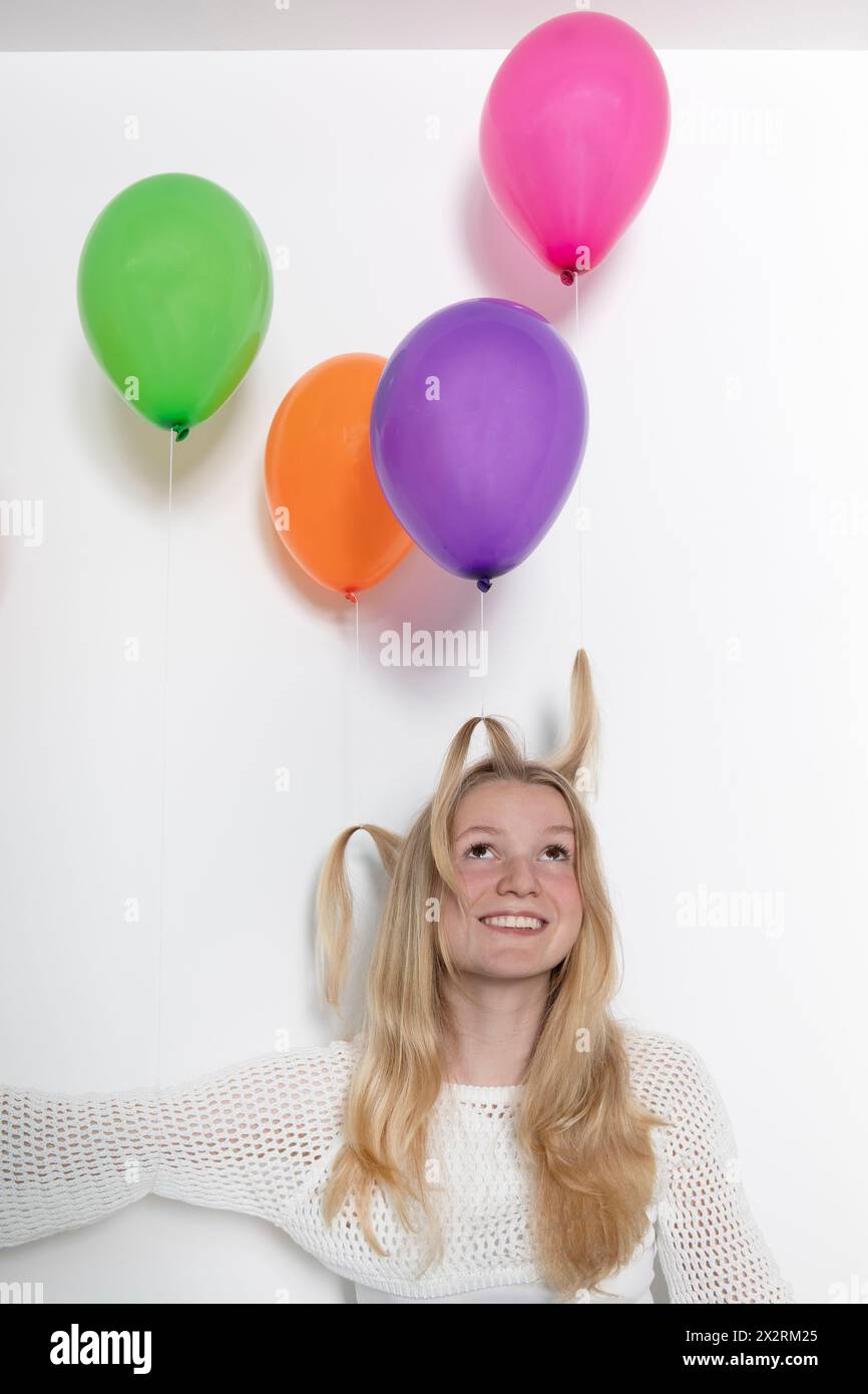 Blond teenage girl with multi colored balloons tied on hair Stock Photo