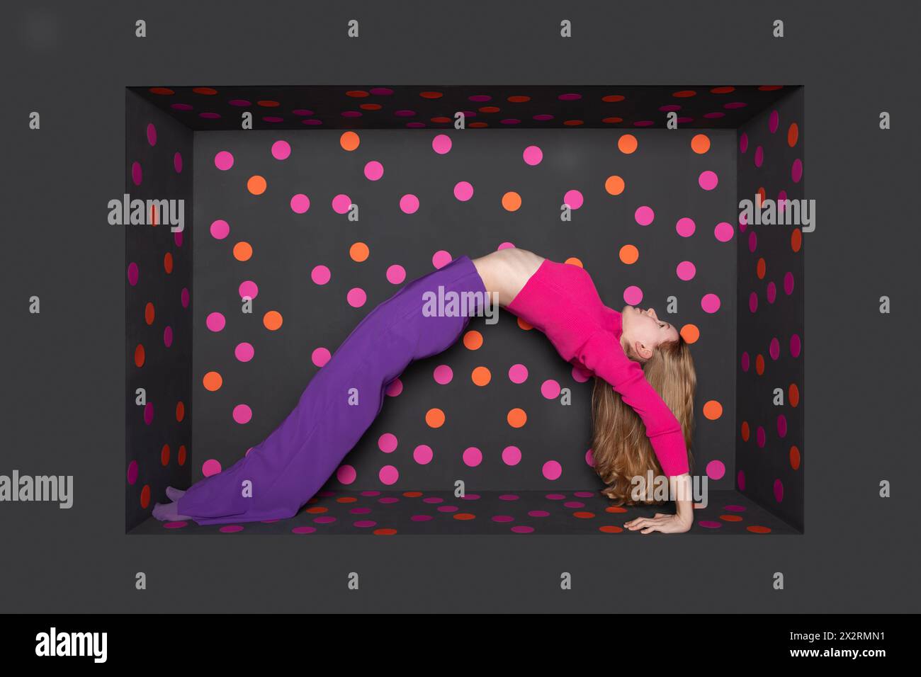 Teenage girl bending backward over black background with colored dots Stock Photo