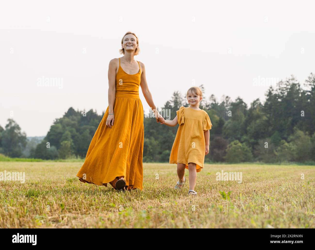Mother and daughter holding hands and walking in meadow Stock Photo