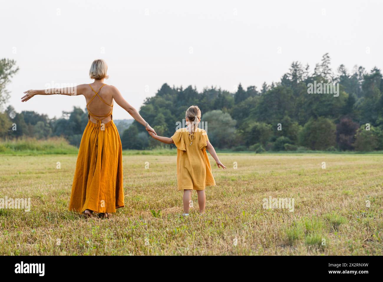 Mother holding hand of daughter and walking in meadow Stock Photo