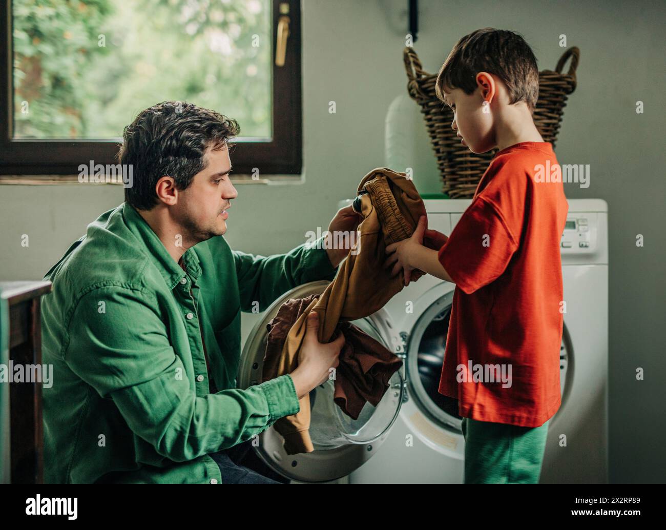 Father and son removing clothes from washing machine at home Stock Photo