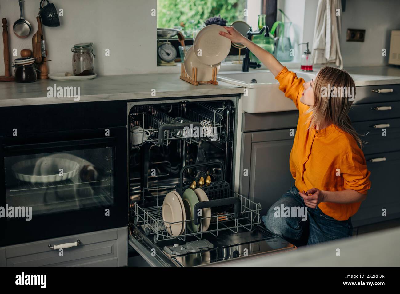 Woman stacking washed plates on kitchen counter at home Stock Photo