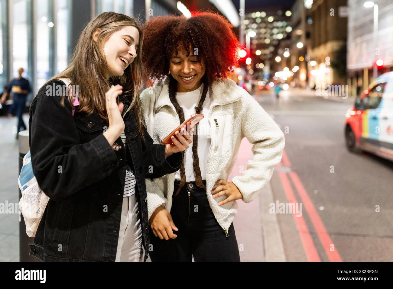 Happy young friends using smart phone on street at night Stock Photo