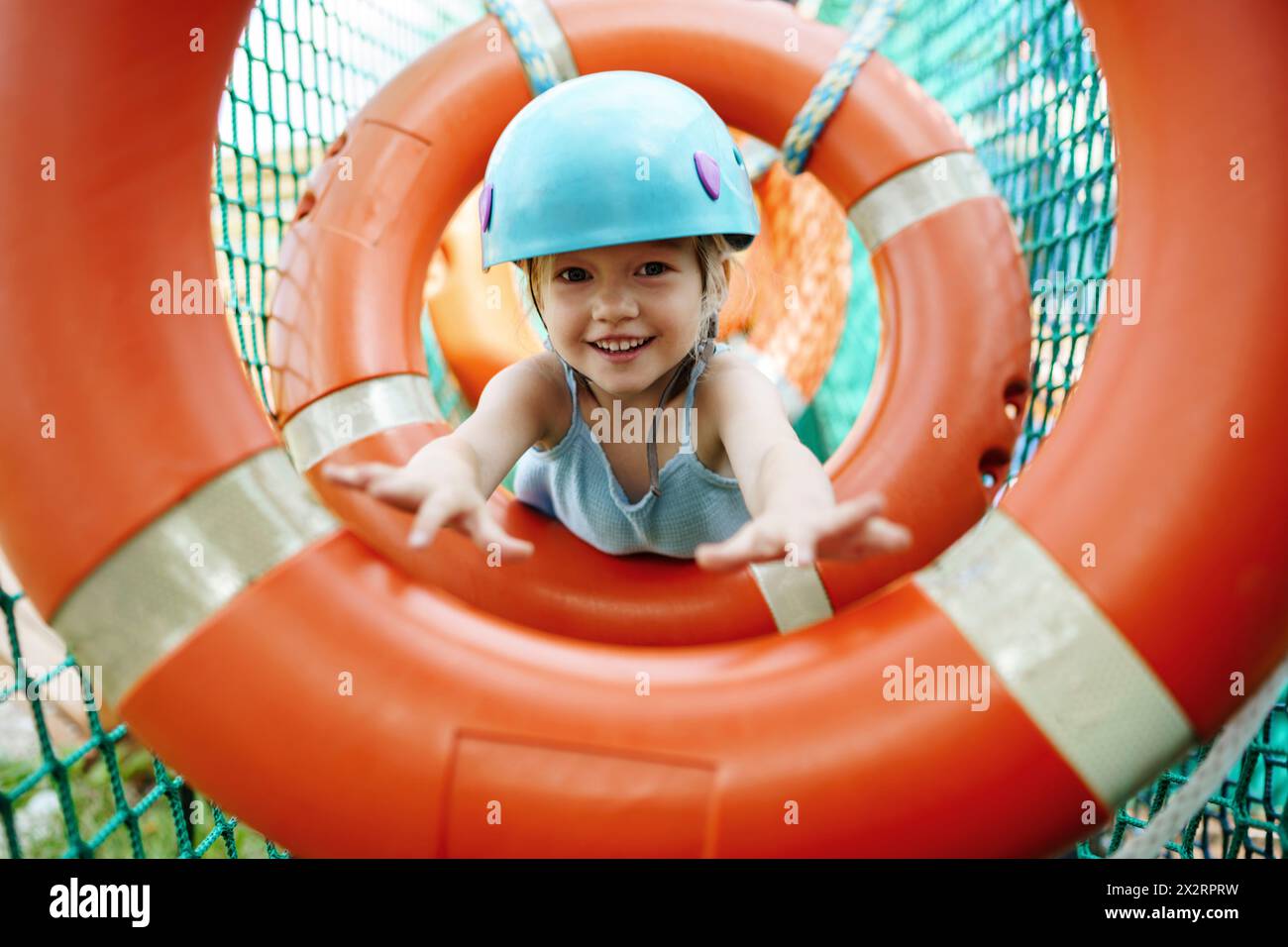 Smiling girl wearing helmet and doing obstacle course at rope park Stock Photo