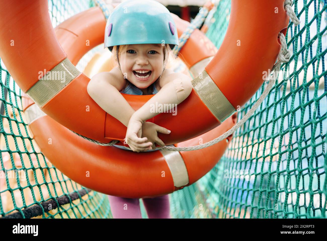 Happy cute girl hanging on circle equipment at rope park Stock Photo