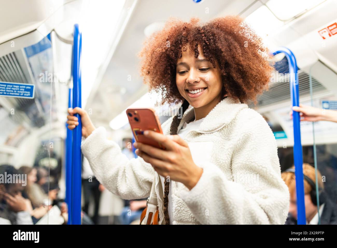 Smiling woman using smart phone in subway train Stock Photo