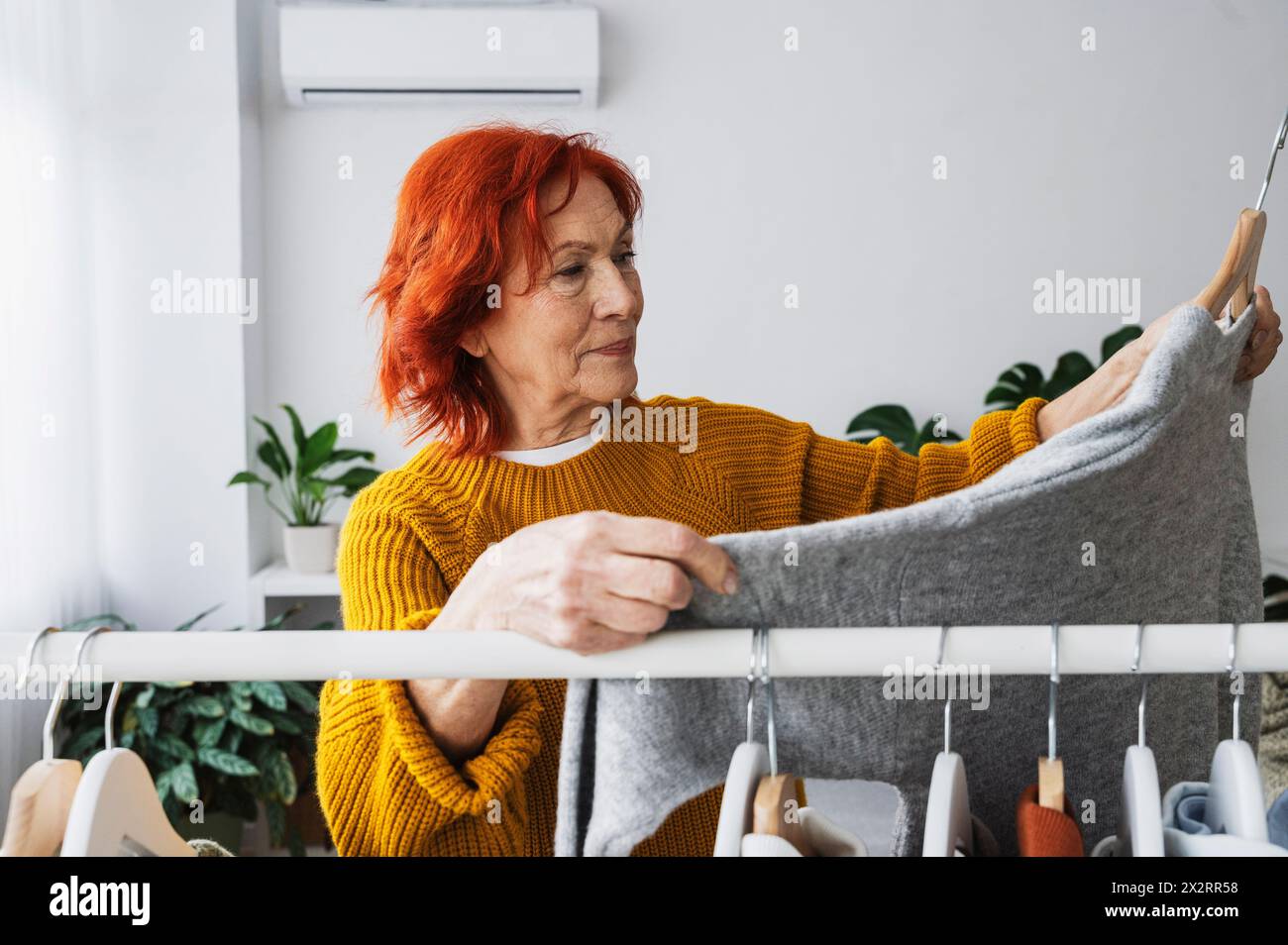 Retired senior woman choosing sweater from clothes rack at home Stock Photo