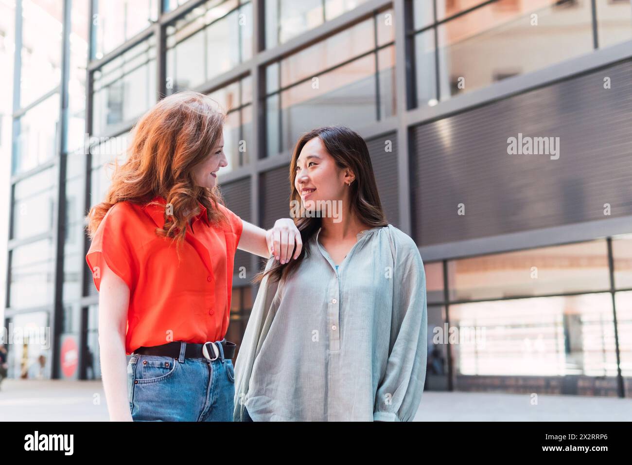 Smiling woman with hand on shoulder of friend near building Stock Photo
