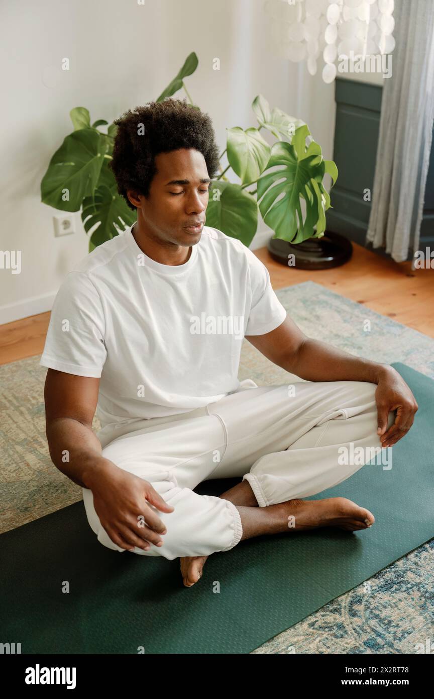 Man Sitting Cross legged On Exercise Mat With Eyes Closed Doing Yoga In man-sitting-cross-legged-on-exercise-mat-with-eyes-closed-doing-yoga-in