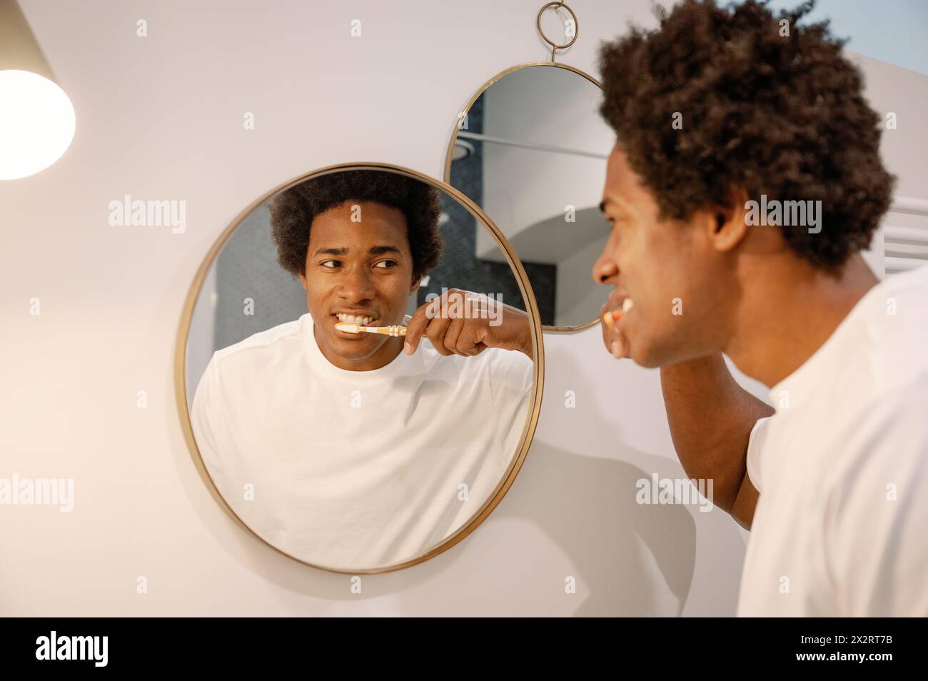 Man brushing teeth looking at mirror reflection in bathroom Stock Photo