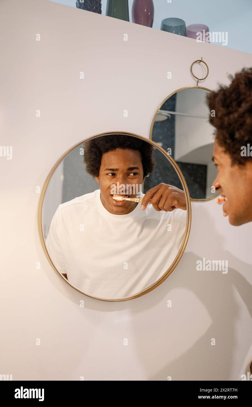 Man brushing teeth looking at reflection on mirror in bathroom Stock Photo