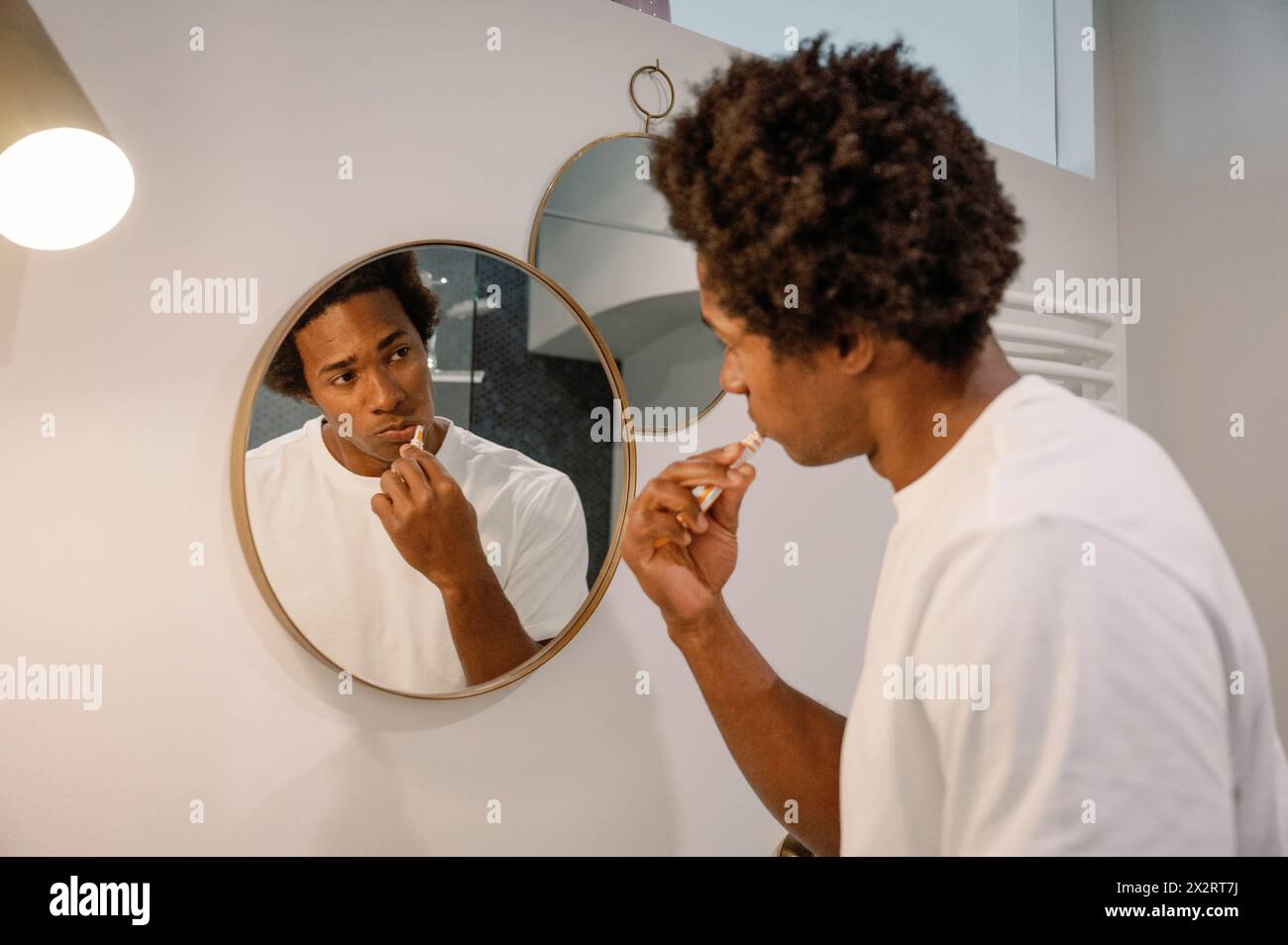 Man brushing teeth looking at mirror in bathroom Stock Photo