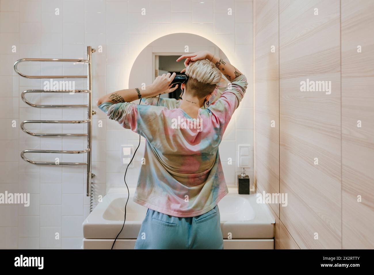 Woman cutting hair with electric razor in bathroom at home Stock Photo