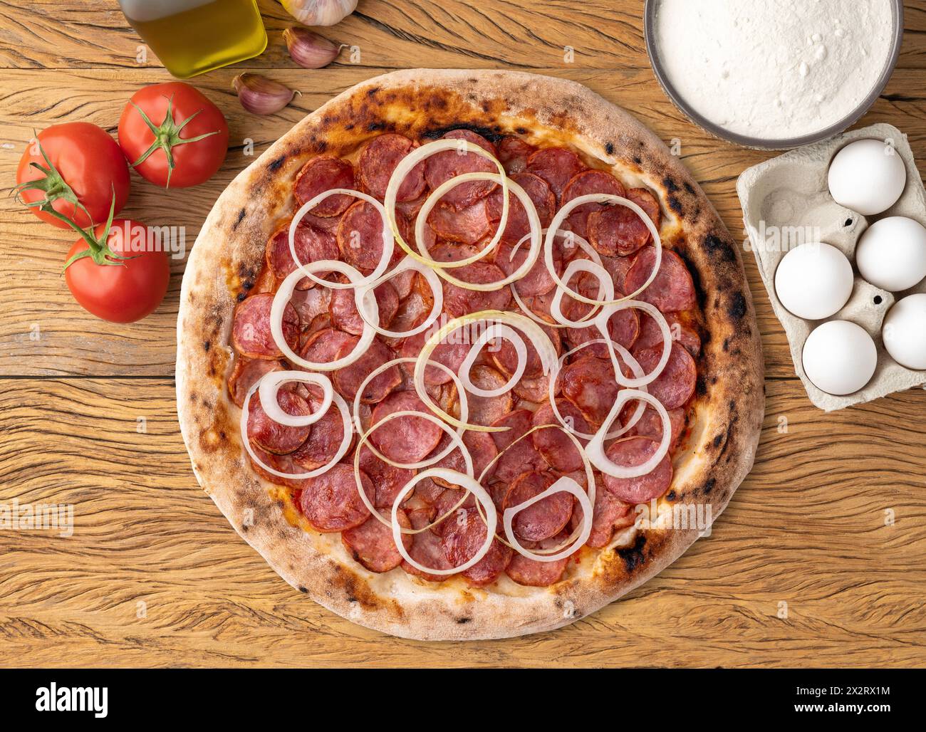Calabrese sausage pizza with tomatoes, olive oil, eggs and flour over wooden table. Stock Photo