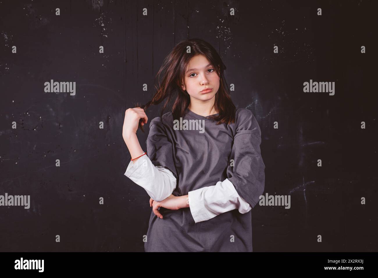 Sad girl holding hair standing in front of black background Stock Photo