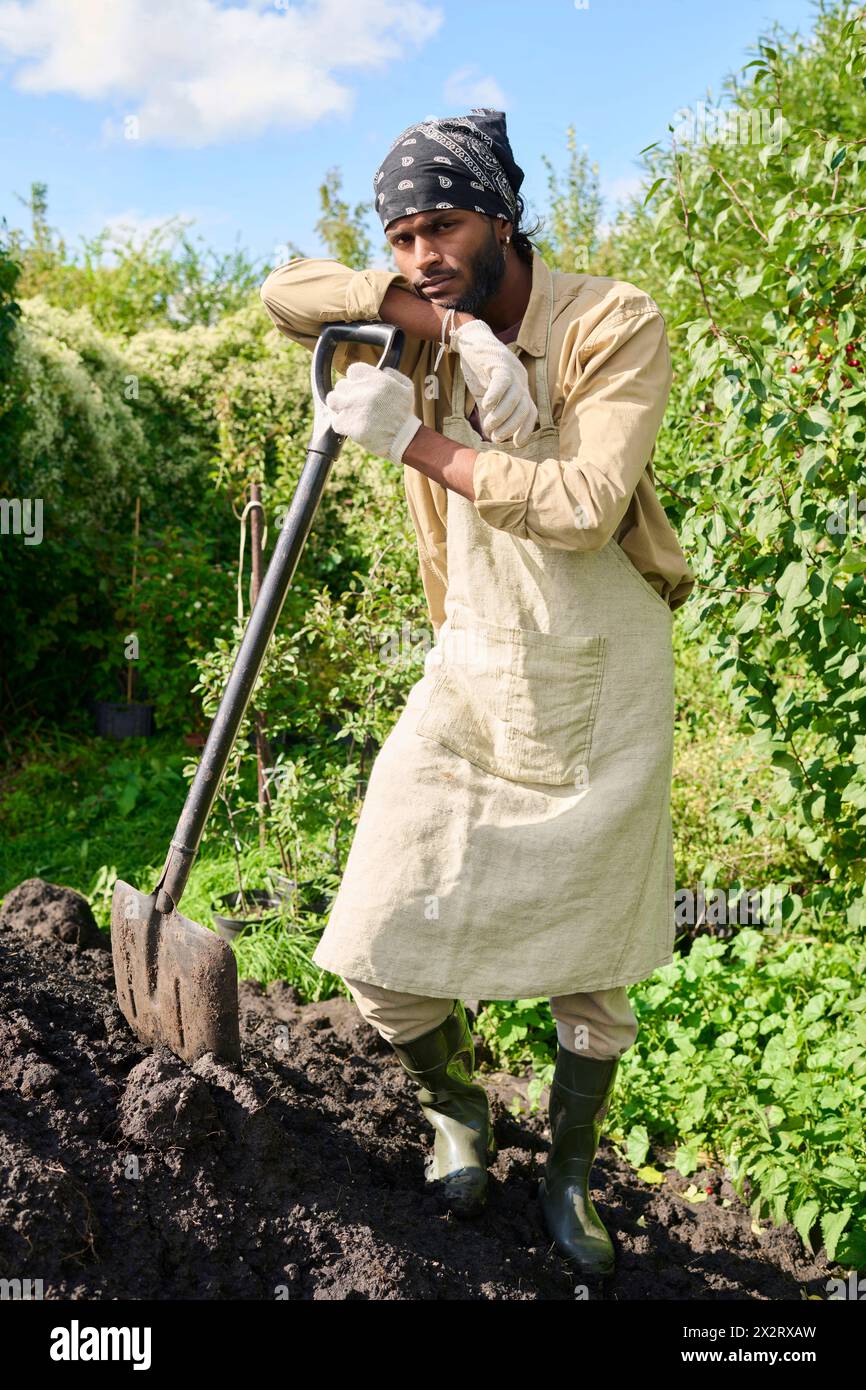 Gardener standing and leaning on shovel in garden Stock Photo