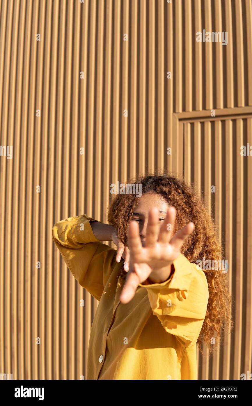 Young woman dancing with obscured face in front of orange wall Stock Photo