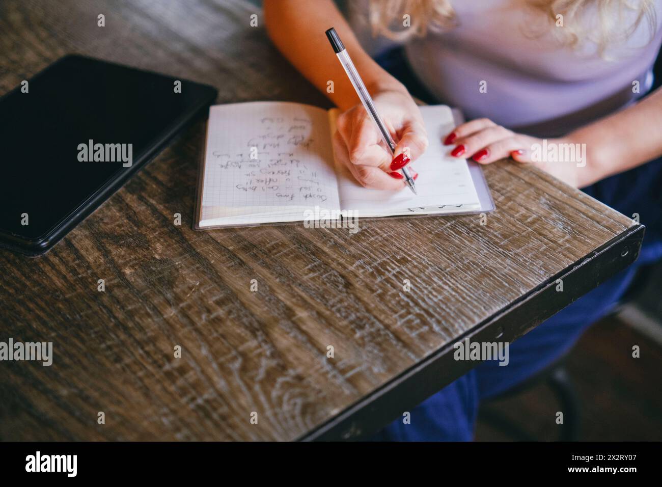 Young woman writing notes in diary at table in cafe Stock Photo
