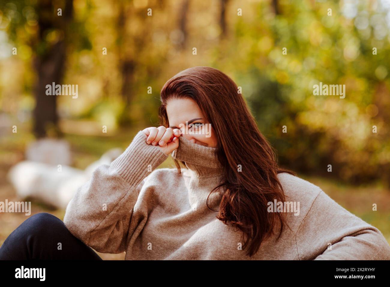 Mature woman covering face with turtleneck t-shirt in park Stock Photo