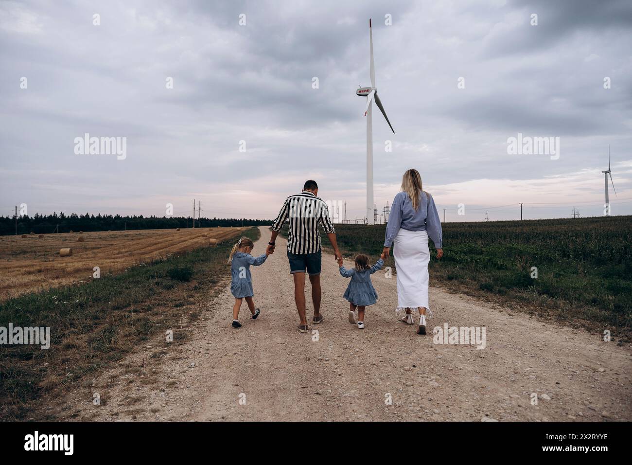 Father and mother holding hands of daughters and walking on dirt road Stock Photo