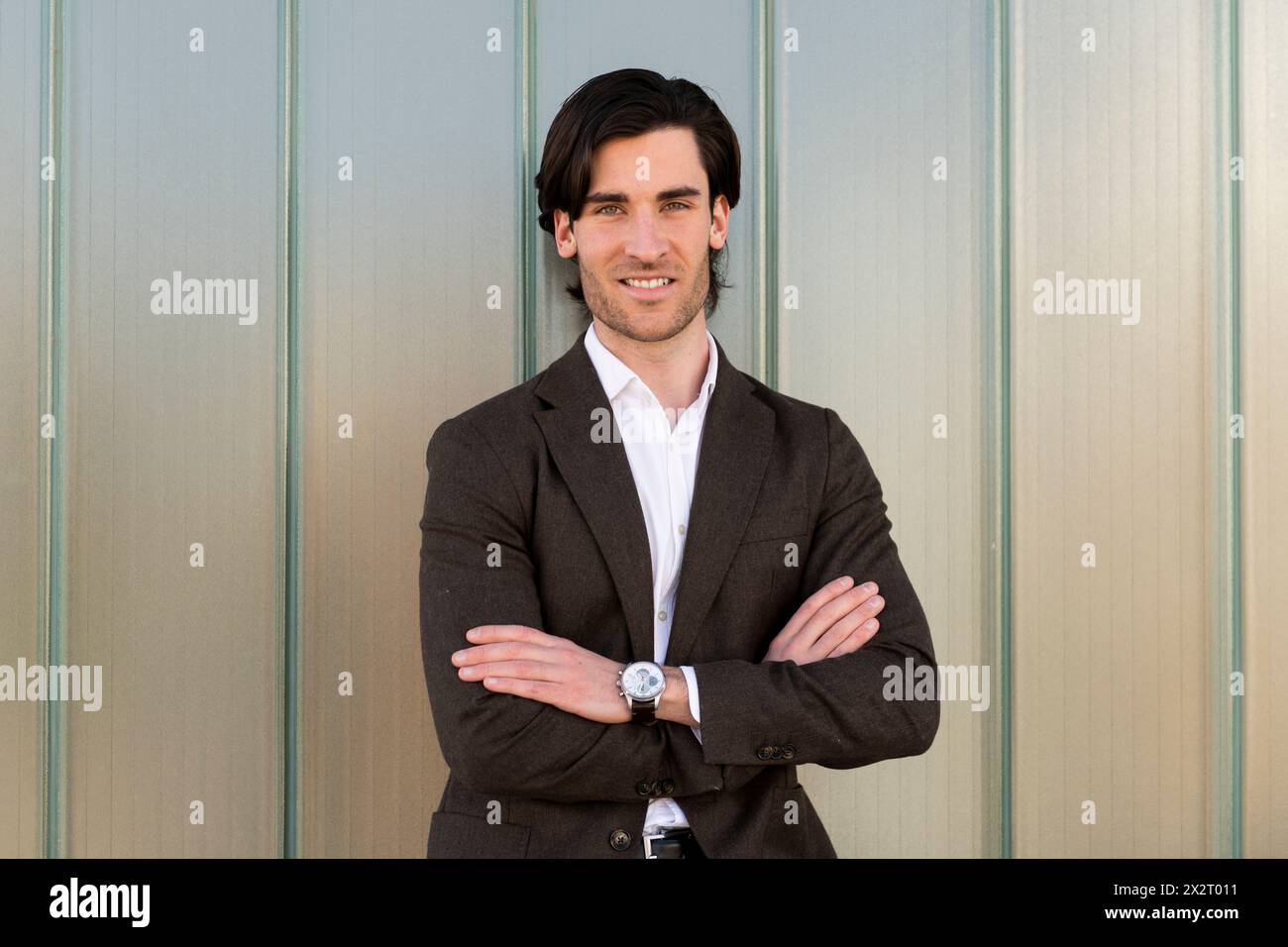 Smiling young businessman with arms crossed in front of wall Stock ...