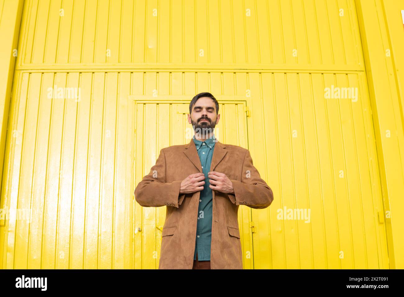 Man wearing brown jacket and standing in front of yellow wall Stock Photo
