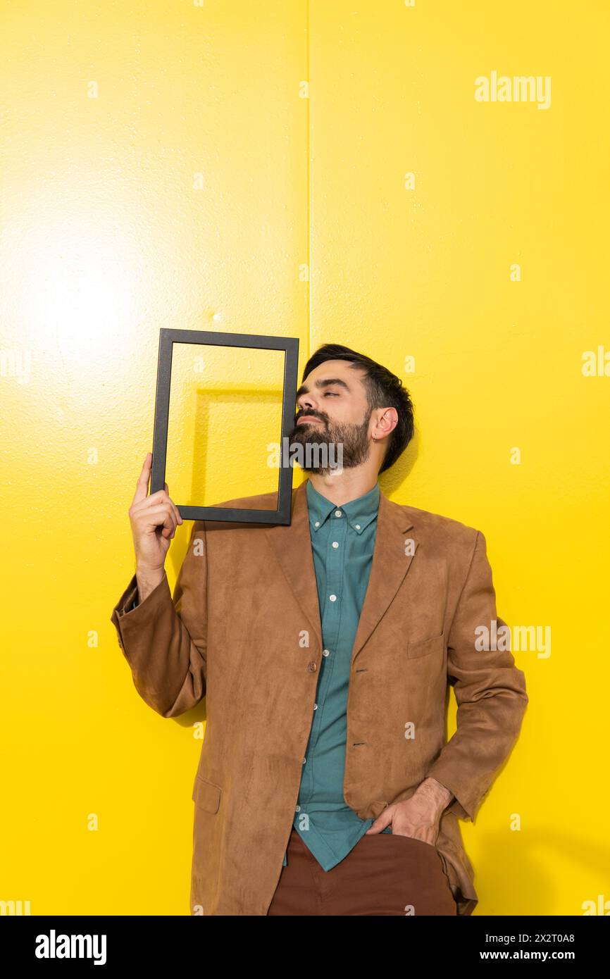 Man standing with picture frame in front of yellow wall Stock Photo