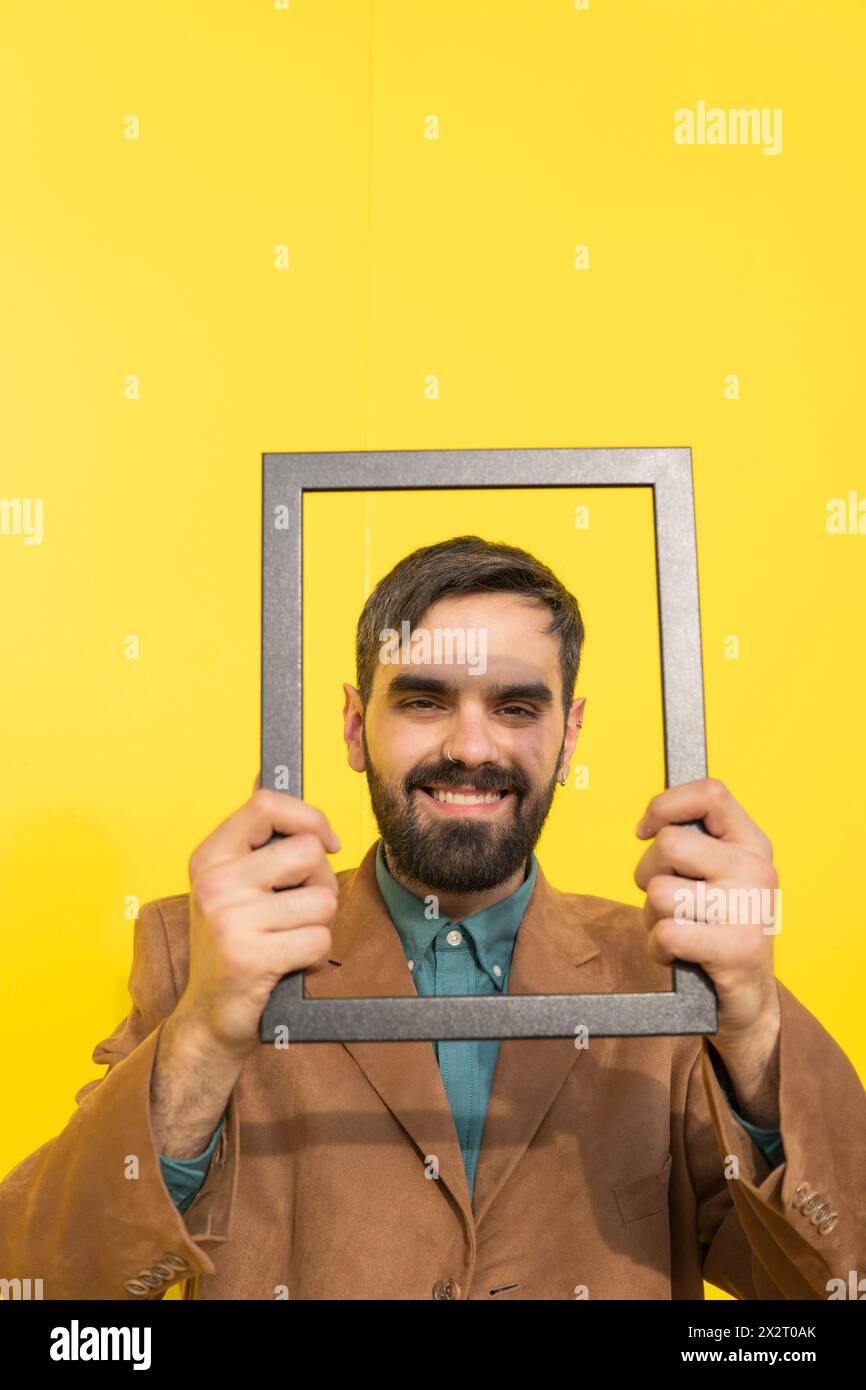 Happy man looking through picture frame against yellow background Stock Photo