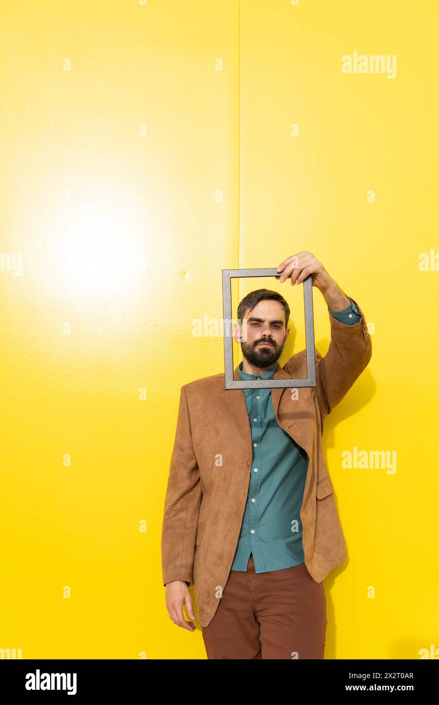 Man looking through picture frame in front of yellow wall Stock Photo