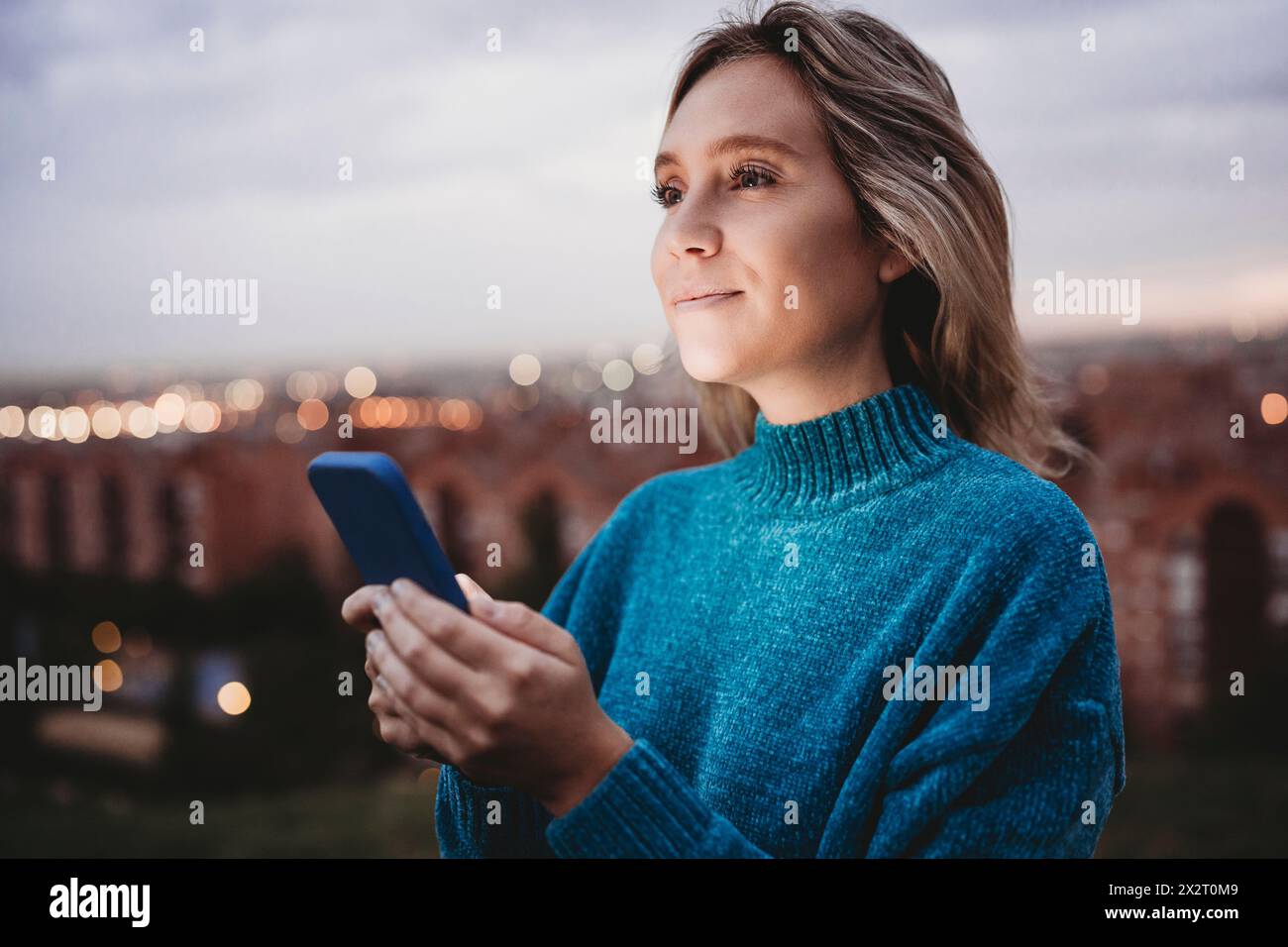 Woman holding smart phone and day dreaming at dusk Stock Photo