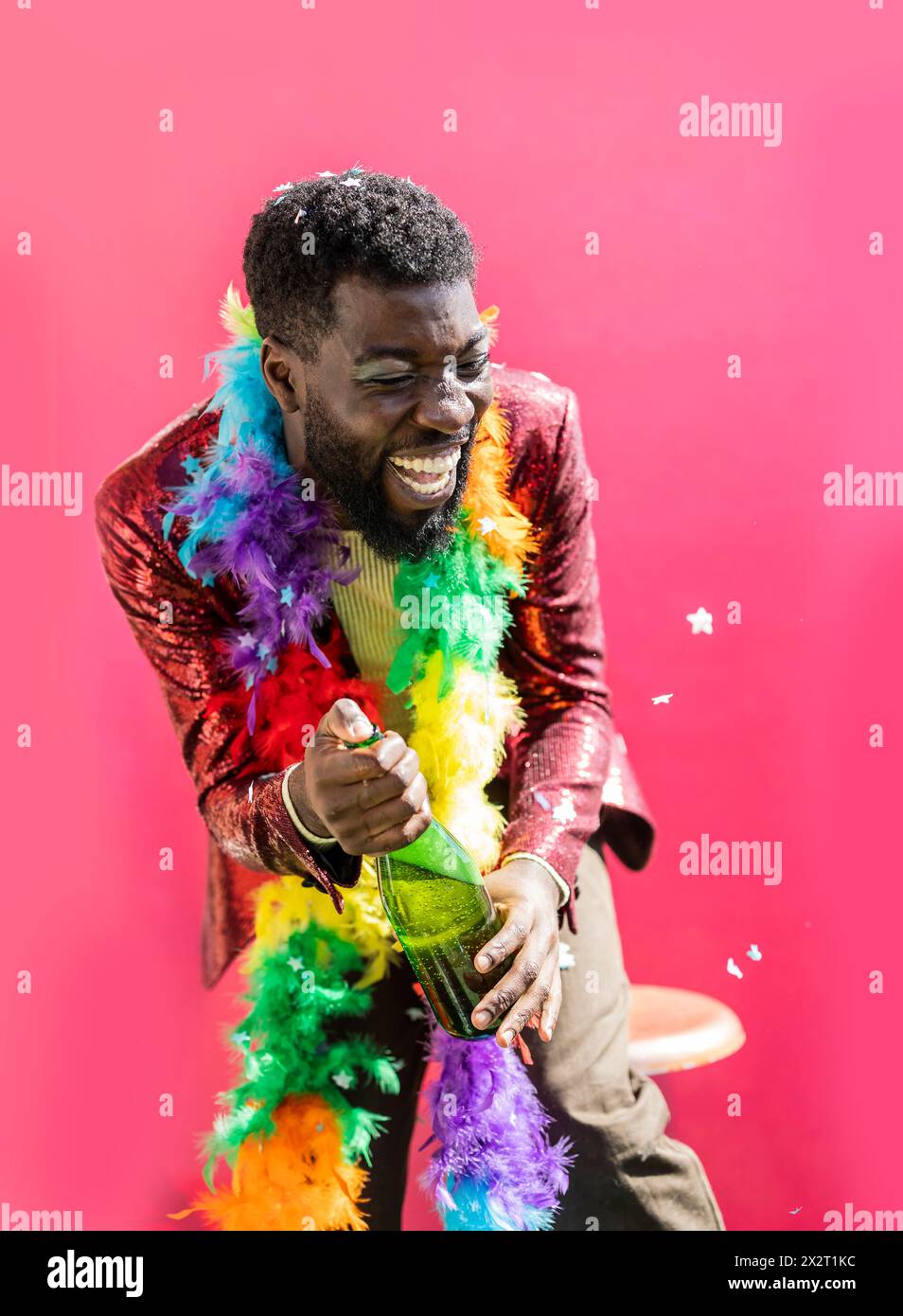 Young non-binary person holding champagne bottle and laughing against pink background Stock Photo