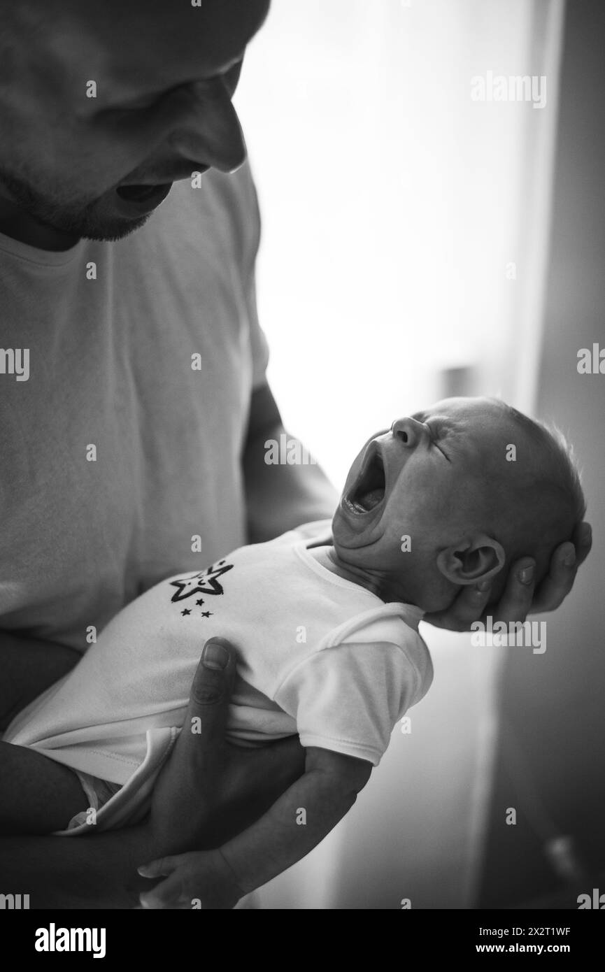 Baby boy crying in father's arms at home Stock Photo