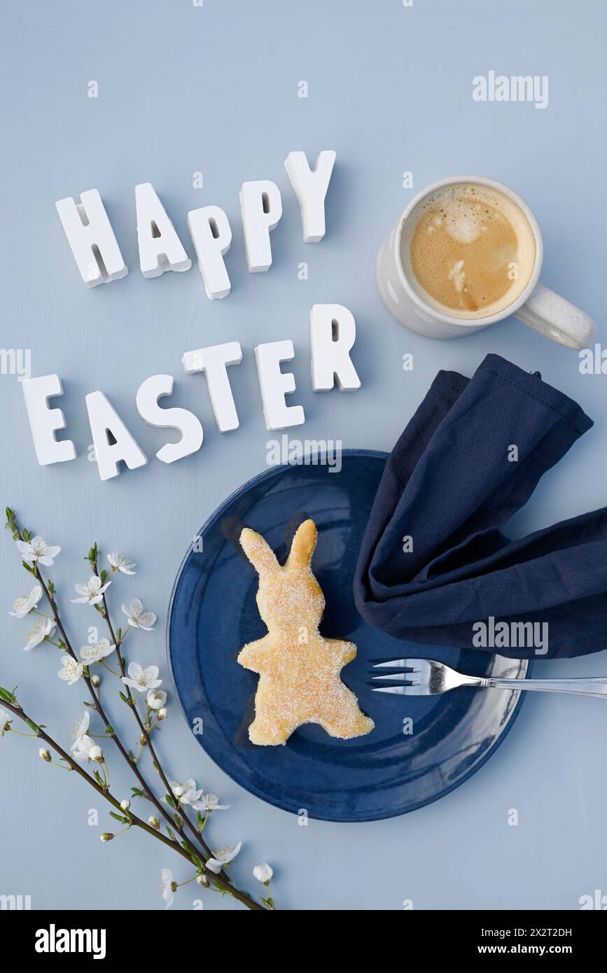 Happy Easter phrase, blackthorn twigs, mug of coffee and bunny shaped cake Stock Photo